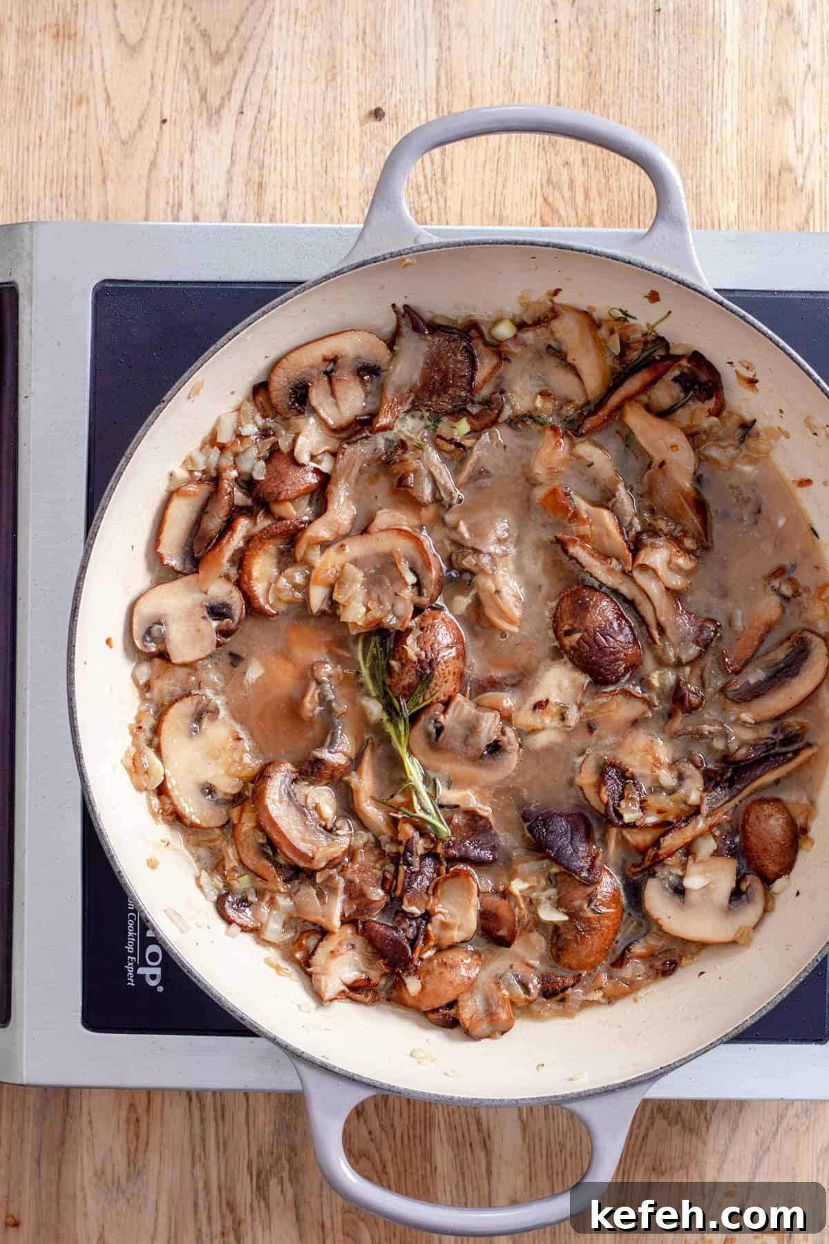 Mushrooms cooking in a large skillet with onions, garlic, herbs and white wine.