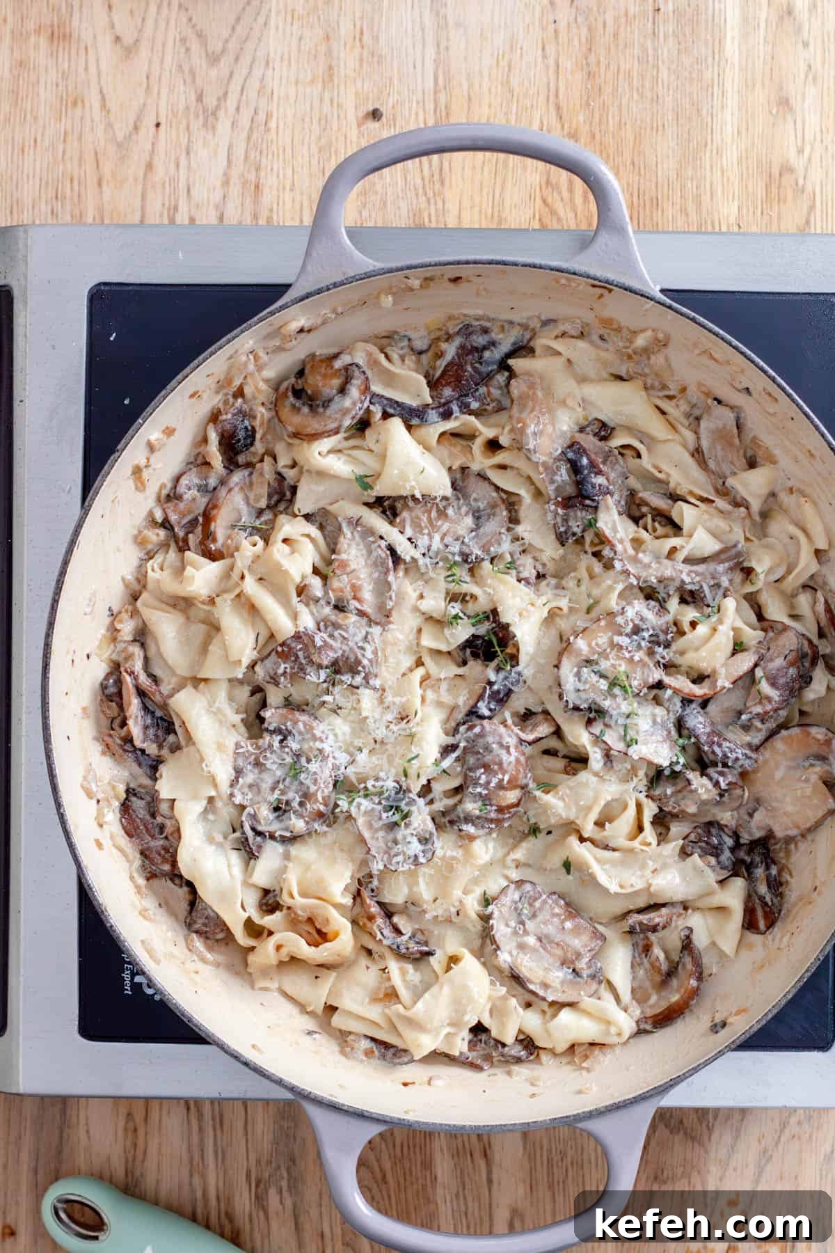 Mushroom pappardelle cooking in a large skillet garnished with parmesan cheese.