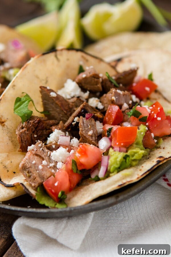 Delicious authentic carne asada taco in a warm corn tortilla with guacamole, red onions and tomatoes on a plate.