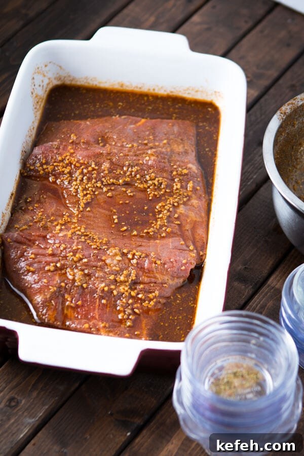 Marinated flank stake in a white casserole dish on top of a wooden table.
