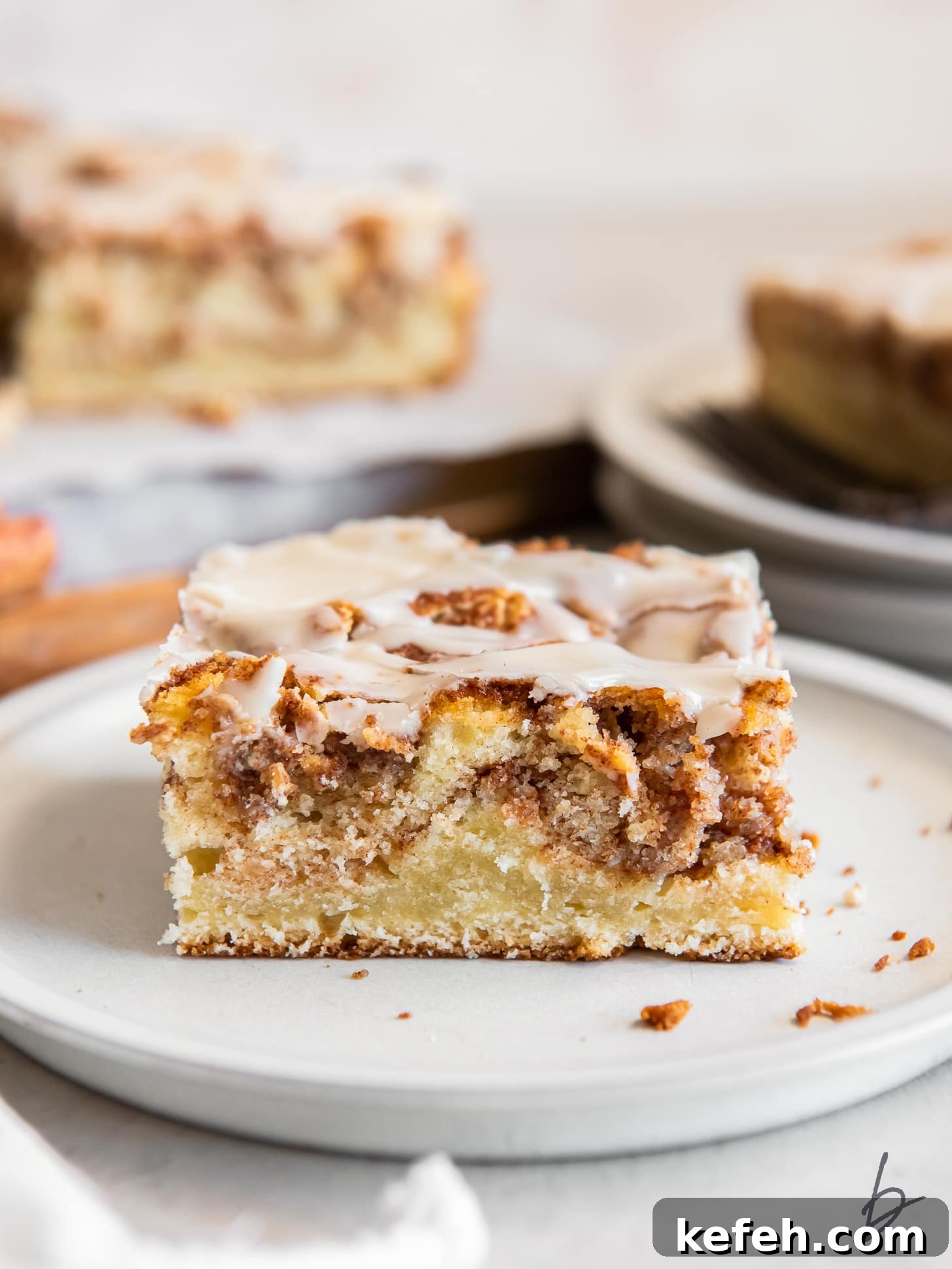 slice of honey bun cake on a plate showing layers of cinnamon brown sugar inside.