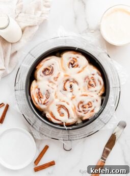 cinnamon rolls with cream cheese icing in round cake pan on round wire rack