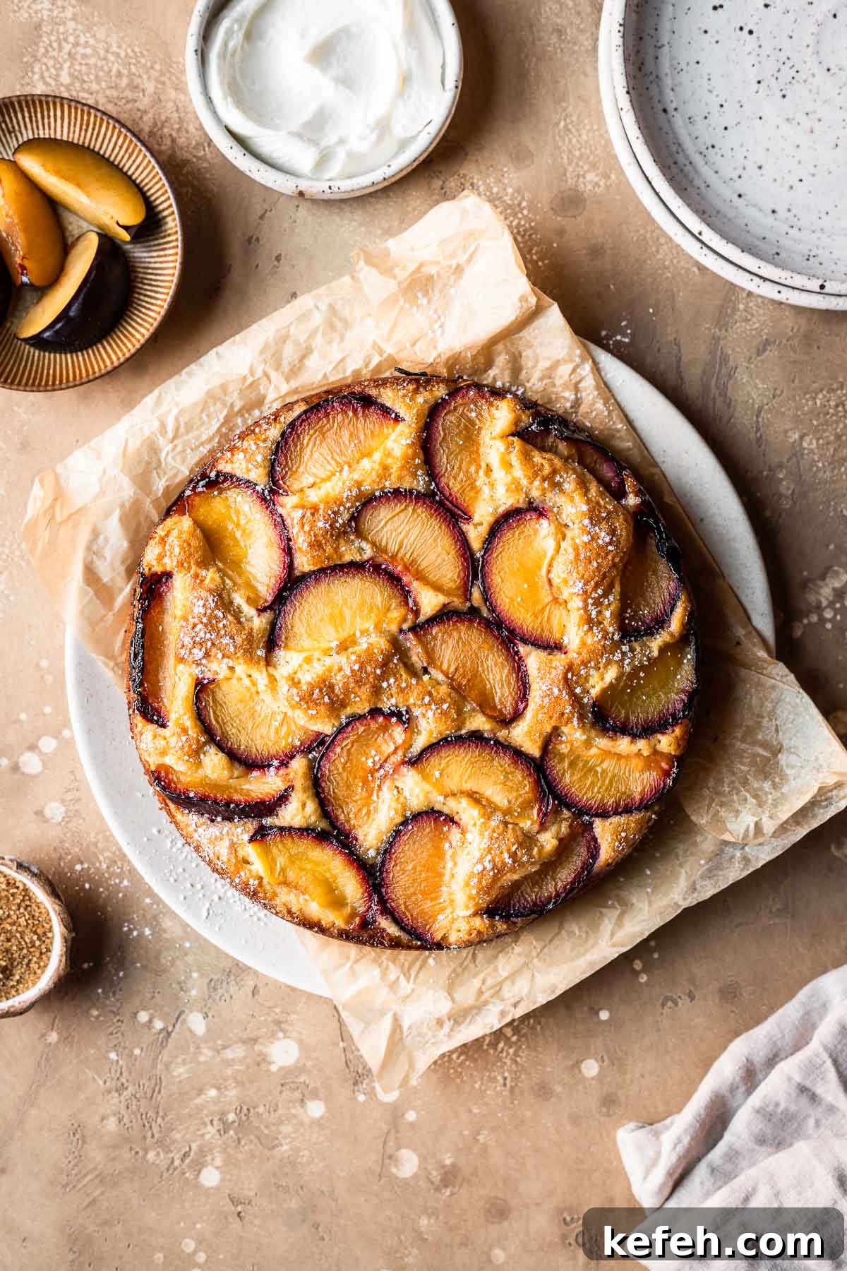 A baked plum yogurt cake on a parchment paper lined platter.