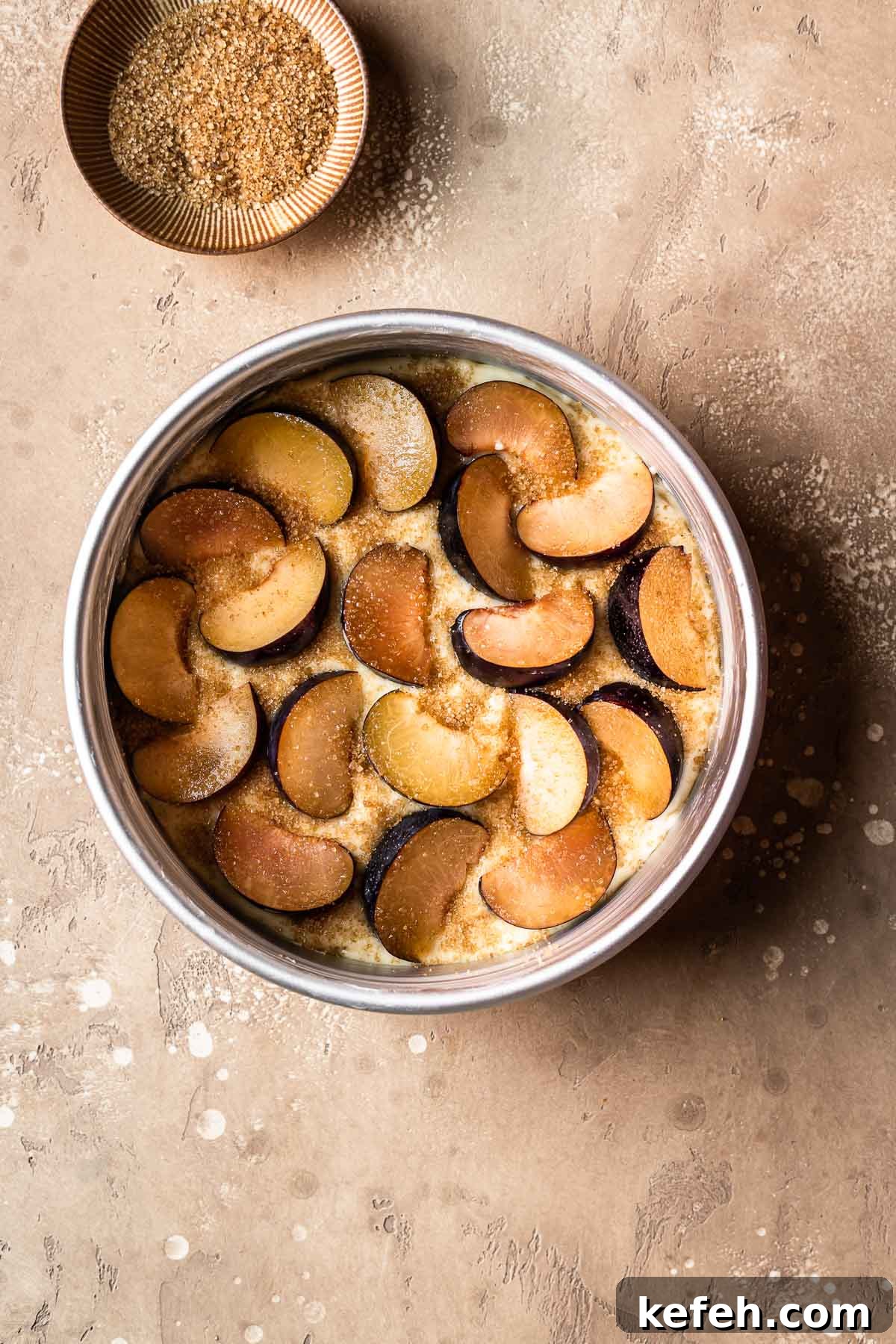Cake batter topped with sliced plums and raw sugar.