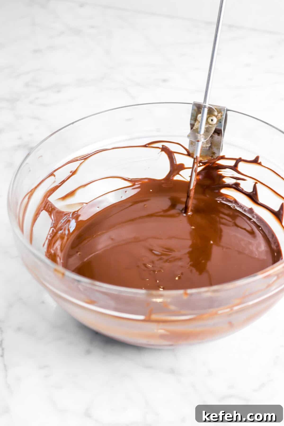 melted chocolate in a glass bowl on a marble counter.