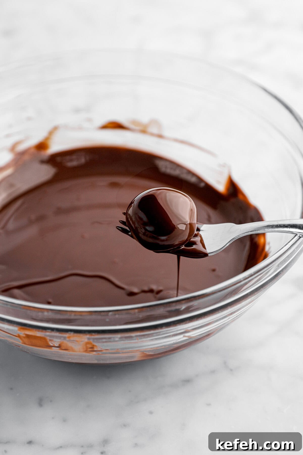 chocolate dipped peanut butter ball on fork over bowl of melted chocolate.