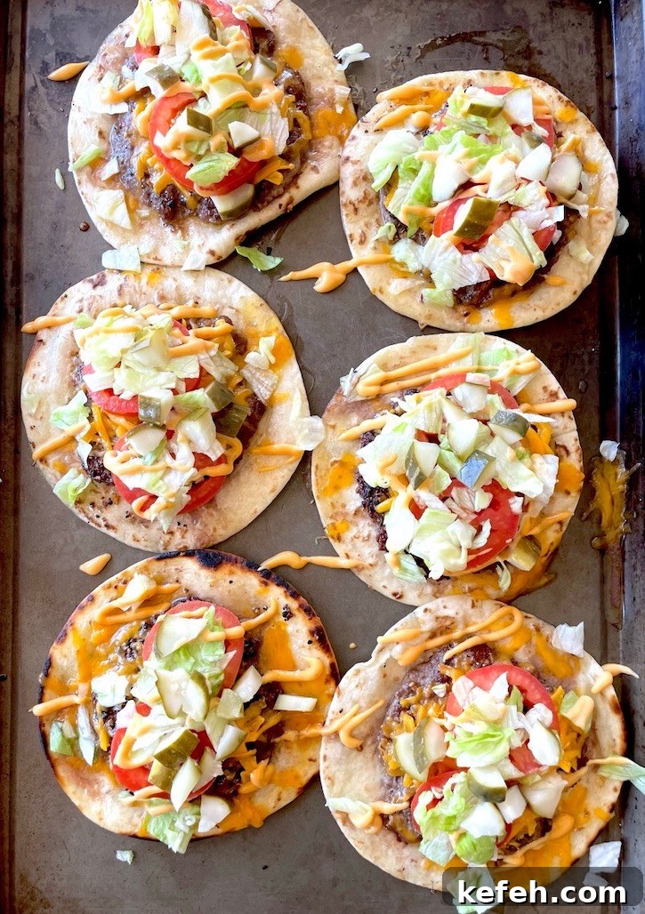 Six Smashed Cheeseburger Tacos on a sheet pan loaded with burger condiments such as lettuce, tomato, pickle, and Bic Mac Sauce. 