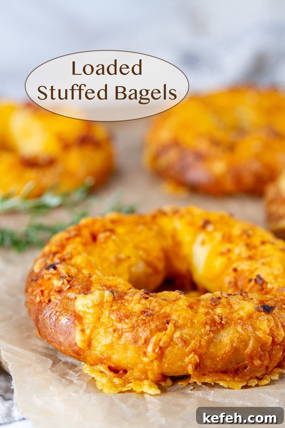 Loaded Stuffed Bagel Recipes: Creative Fillings and Toppings 2 bagels topped with cheddar cheese on parchment paper with fresh rosemary in the background.
