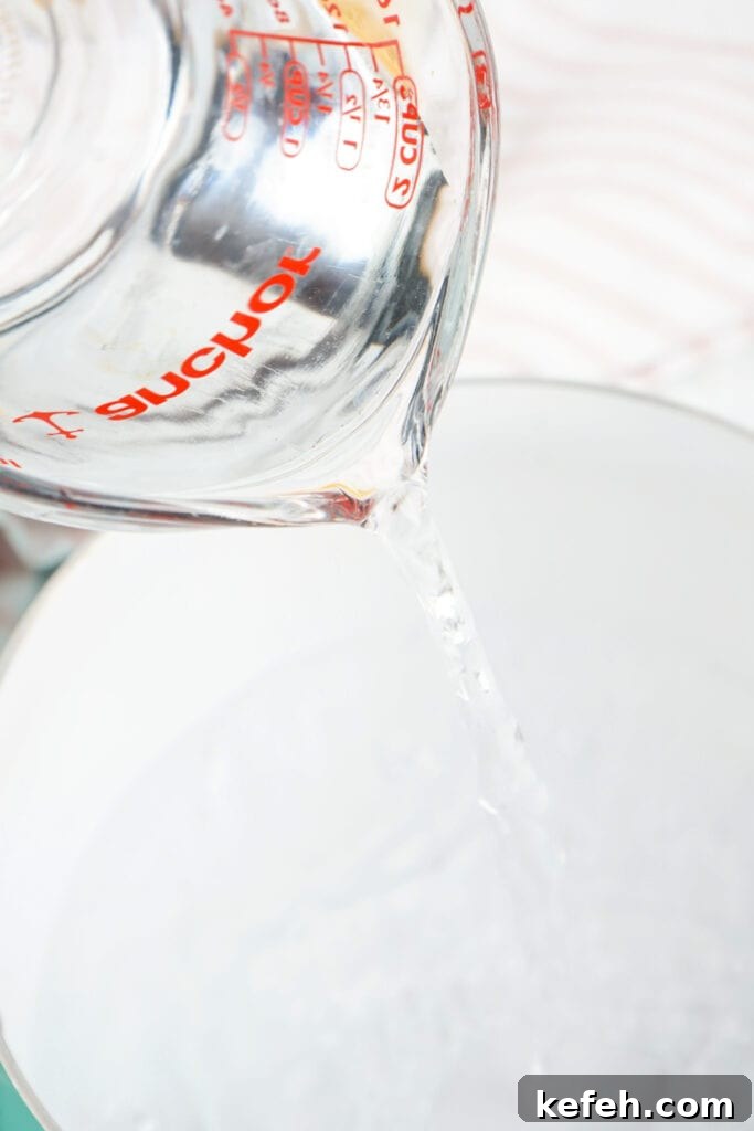 Water being poured from a glass measuring cup into a saucepan for melting ingredients.