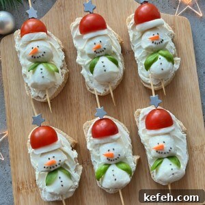 Christmas Party Appetizer Ideas to Impress Your Guests 12 Six slices of bread topped with cream cheese, shaped like snowmen using cherry tomatoes for hats and veggies for details—these festive bites make delightful Christmas Party Appetizers, beautifully arranged on a wooden board.
