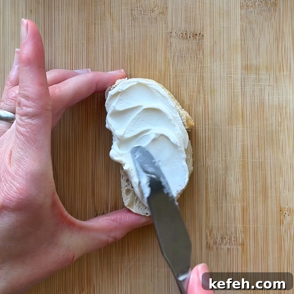 Christmas Party Appetizer Ideas to Impress Your Guests 4 A hand spreads cream cheese on a slice of bread using a butter knife.