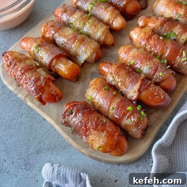 Christmas Party Appetizer Ideas to Impress Your Guests 10 Mini sausages wrapped in crispy bacon are arranged on a wooden board, garnished with chopped herbs, next to a dipping sauce.