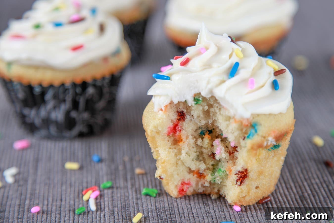 a Funfetti cupcake with vanilla frosting and sprinkles with a bite taken out of it. 