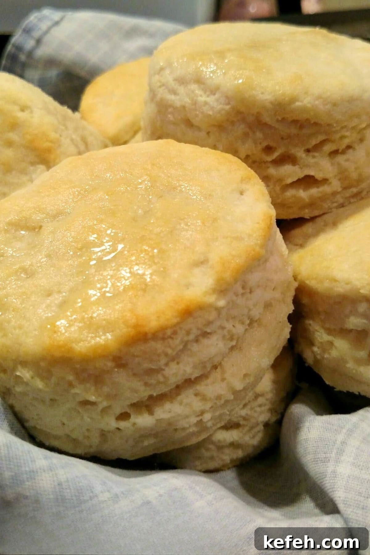 Flaky Buttermilk Biscuits Recipe for Perfect Homemade Biscuits 2 A close-up of freshly baked, golden brown biscuits stacked in a basket lined with a blue and white cloth, showcasing the fluffy texture and glossy tops from this classic Buttermilk Biscuit Recipe.