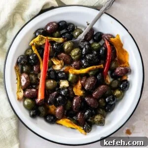Round white dish with roasted olives, and a silver spoon sitting in it.