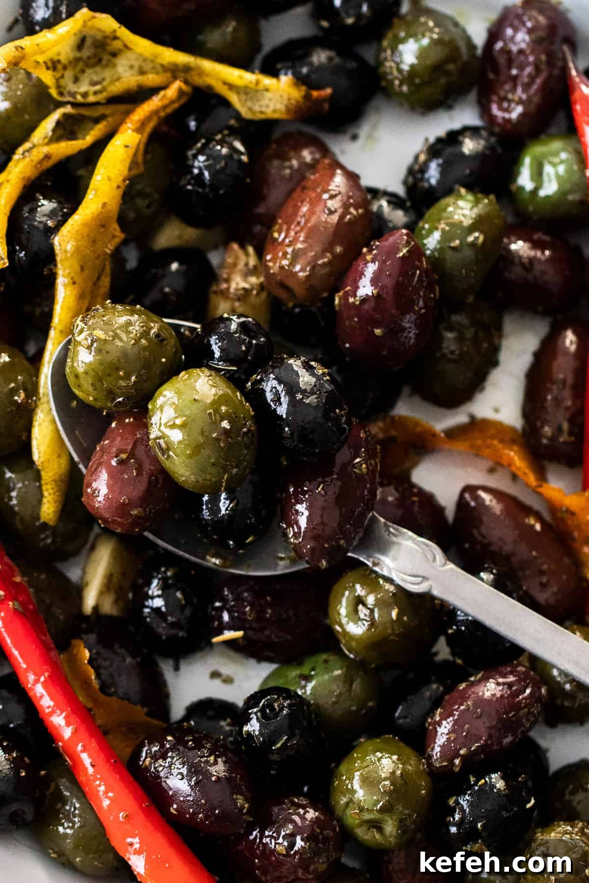 Up close shot of dish with roasted olives, and a silver spoon sitting in it.