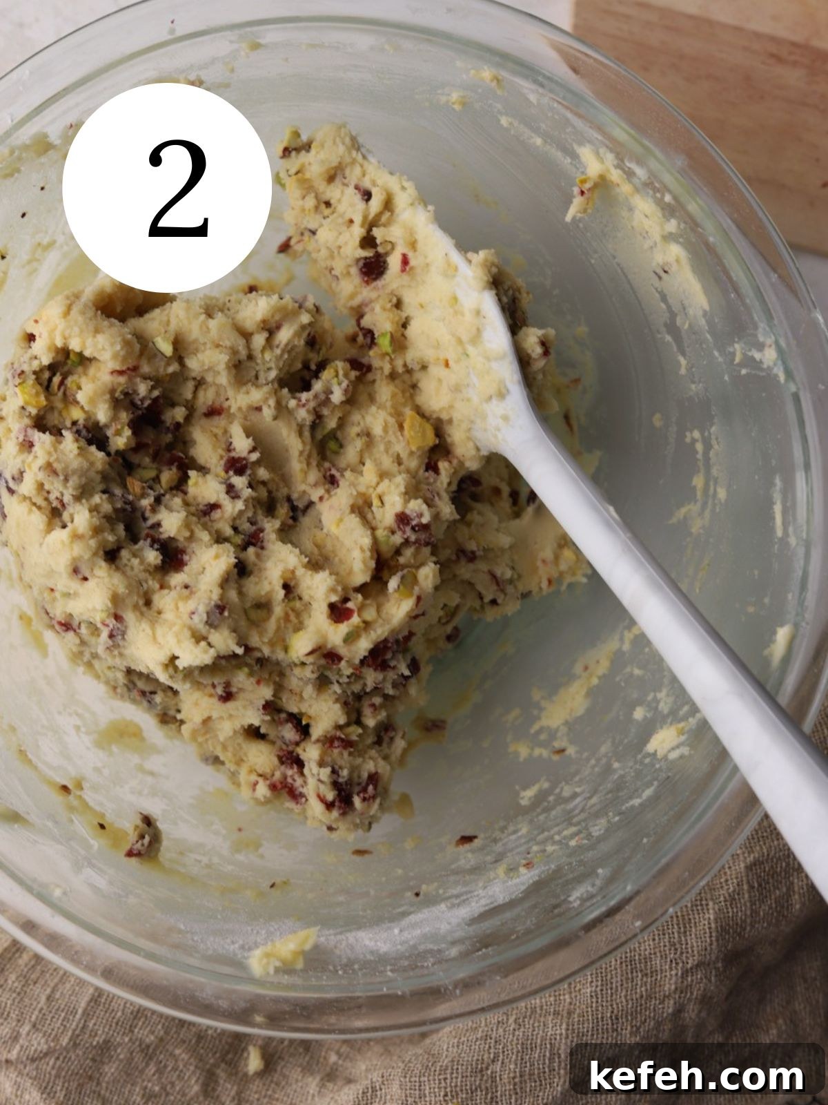 Cranberry Shortbread Cookies Recipe — Buttery Holiday Treat 5 Stirring chopped nuts and cranberries into cookie dough in a glass bowl.
