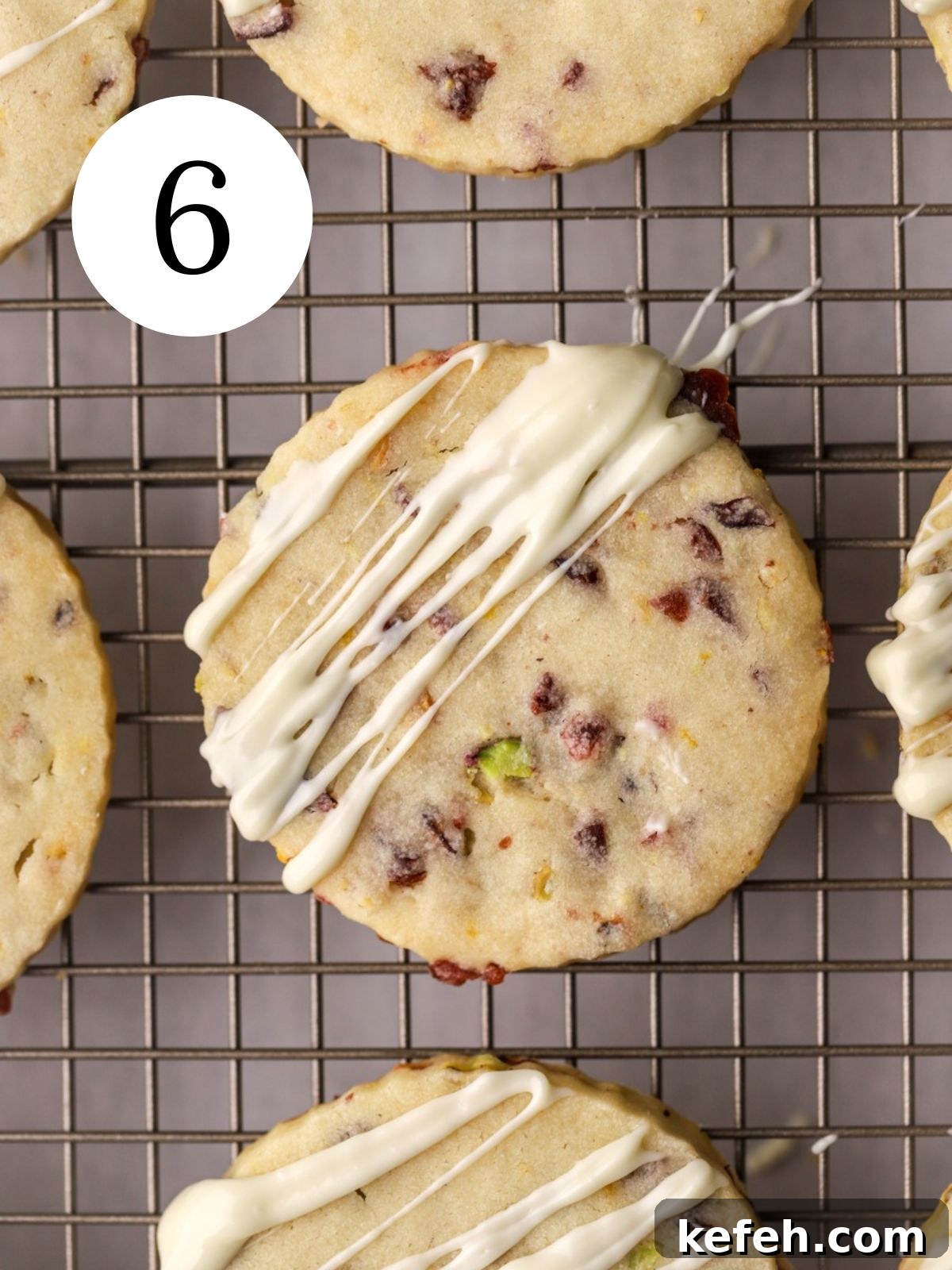 Cranberry Shortbread Cookies Recipe — Buttery Holiday Treat 9 Cranberry shortbread cookies with white chocolate drizzled on top set on a wire rack.
