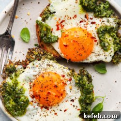 Two fried eggs with pesto on toast, seasoned with chili flakes and pepper.