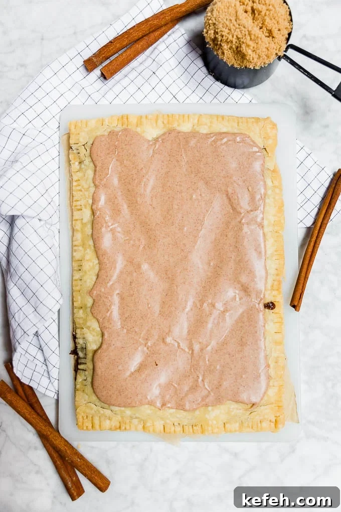 A giant sized gluten-free vegan brown sugar cinnamon pop tart with cinnamon sticks and a cup of brown sugar.