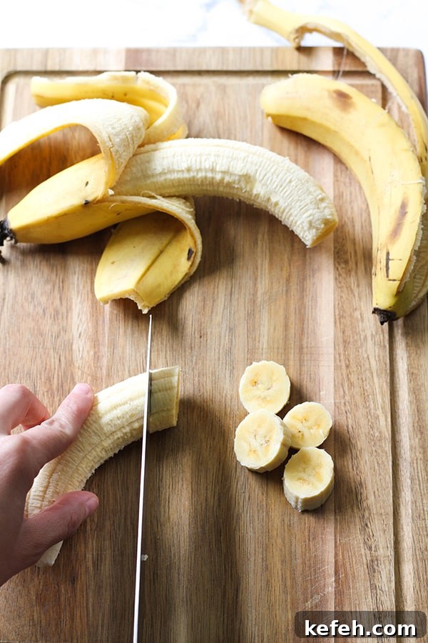 banana being sliced on a wooden cutting board.