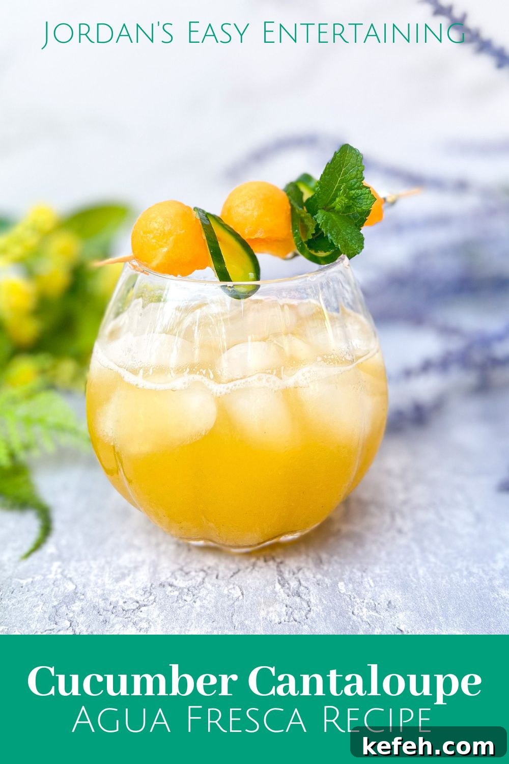 a glass of cucumber melon water aka cucumber cantaloupe agua fresca garnished with melon balls, cucumber ribbons and mint leaves