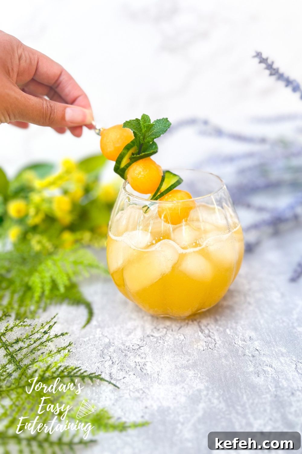 adding garnish of mint, cucumber ribbons and melon calls to a summer mocktail melon water also known as cucumber cantaloupe agua fresca