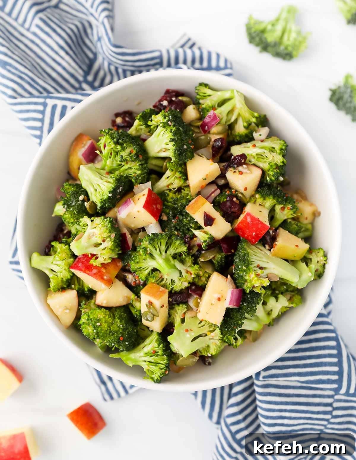 Crispy Broccoli Crunch Salad with Bacon and Sunflower Seeds 2 An overhead picture of broccoli, apples, cranberries, and red onion in a white bowl.