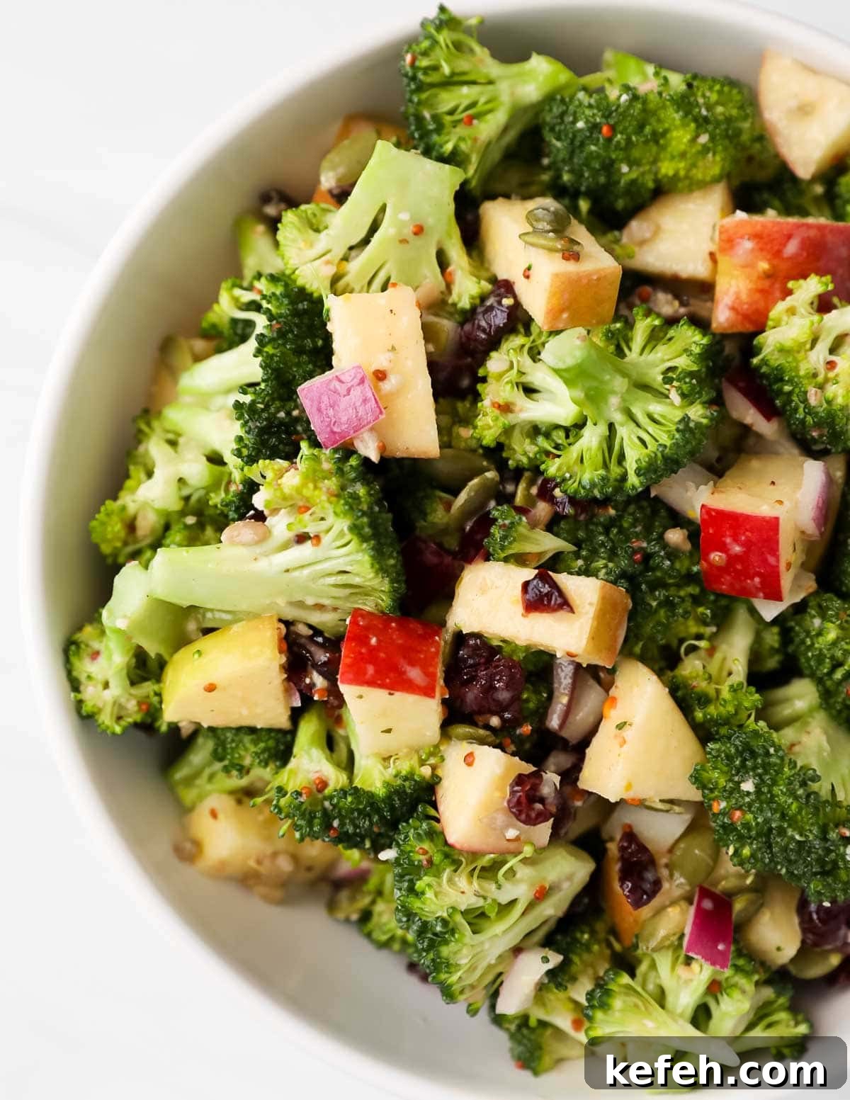 Crispy Broccoli Crunch Salad with Bacon and Sunflower Seeds 6 A close up image of broccoli, apples, onion, and cranberries in a bowl.