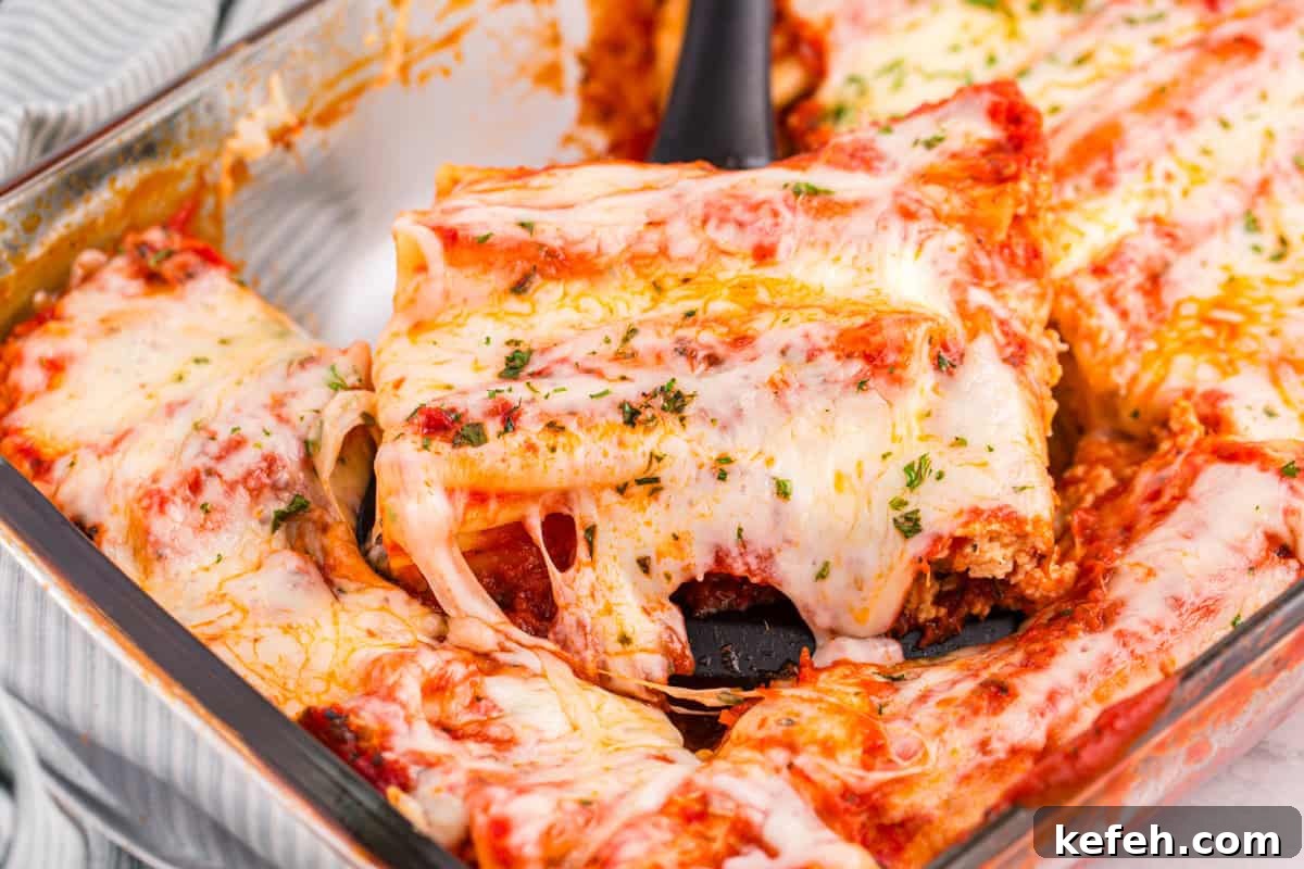 Classic Baked Manicotti with Ricotta and Marinara 11 A spatula lifting a serving of baked cheese manicotti from the dish, with melted cheese stretching and filling visible inside the pasta tubes.