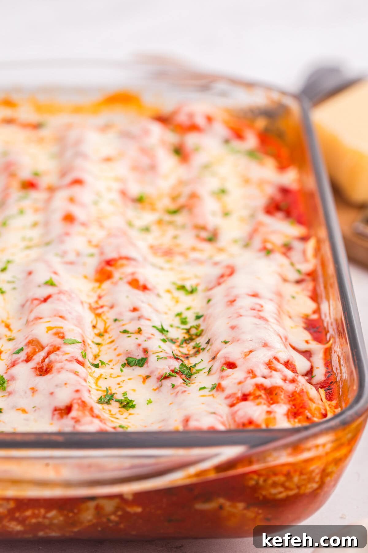 Classic Baked Manicotti with Ricotta and Marinara 12 Close-up of cheesy baked manicotti in a glass dish.