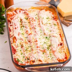 Classic Baked Manicotti with Ricotta and Marinara 13 Baked manicotti covered in tomato sauce, melted mozzarella cheese, and garnished with chopped parsley in a glass baking dish. The cheese is slightly browned and bubbly on top.