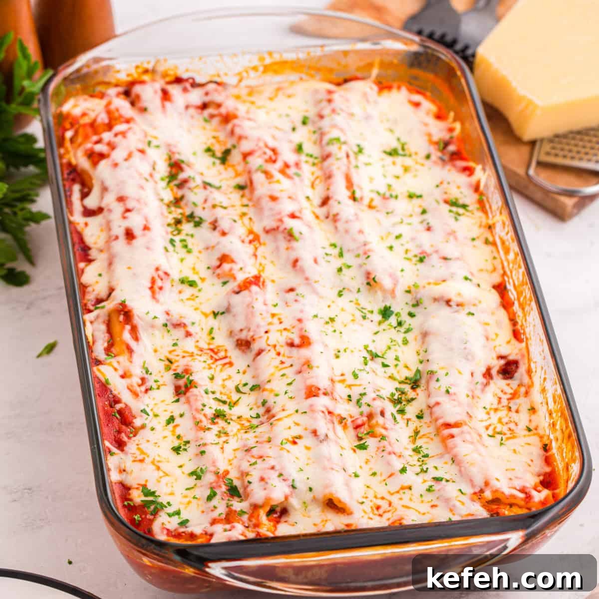 Classic Baked Manicotti with Ricotta and Marinara 3 Baked manicotti covered in tomato sauce, melted mozzarella cheese, and garnished with chopped parsley in a glass baking dish. The cheese is slightly browned and bubbly on top.