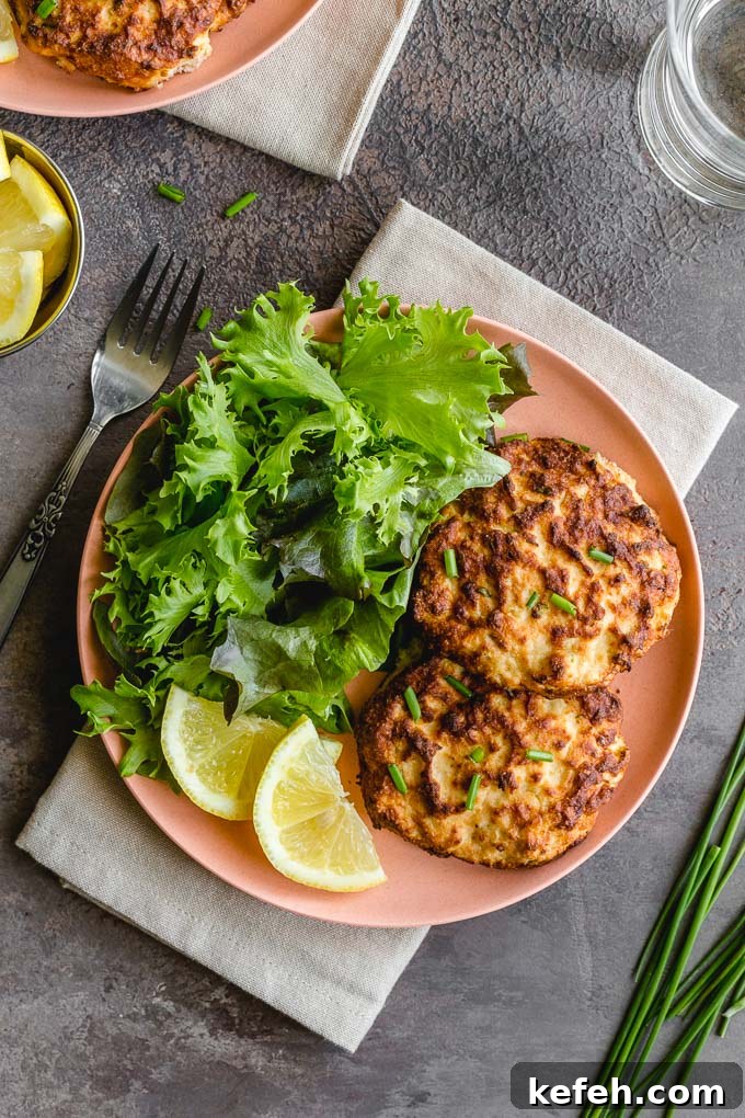Two air fryer salmon cakes on a pink plate with leafy greens and lemon slices.