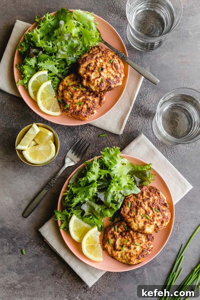 Overhead view of two plates with salmon patties and greens and glasses of water off to the side.