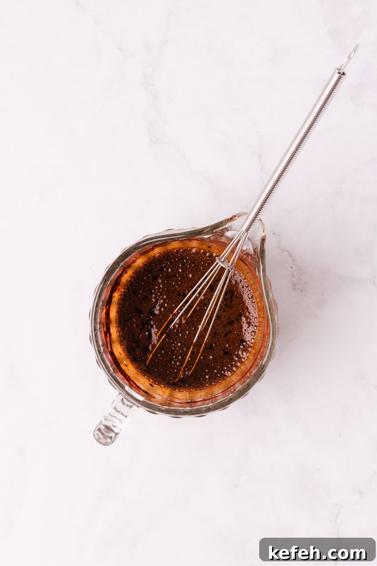 Creamy Mocha Milkshake Recipe for Coffee Lovers 5 A small glass jug with coffee and cocoa mixed together, with a small metal whisk.