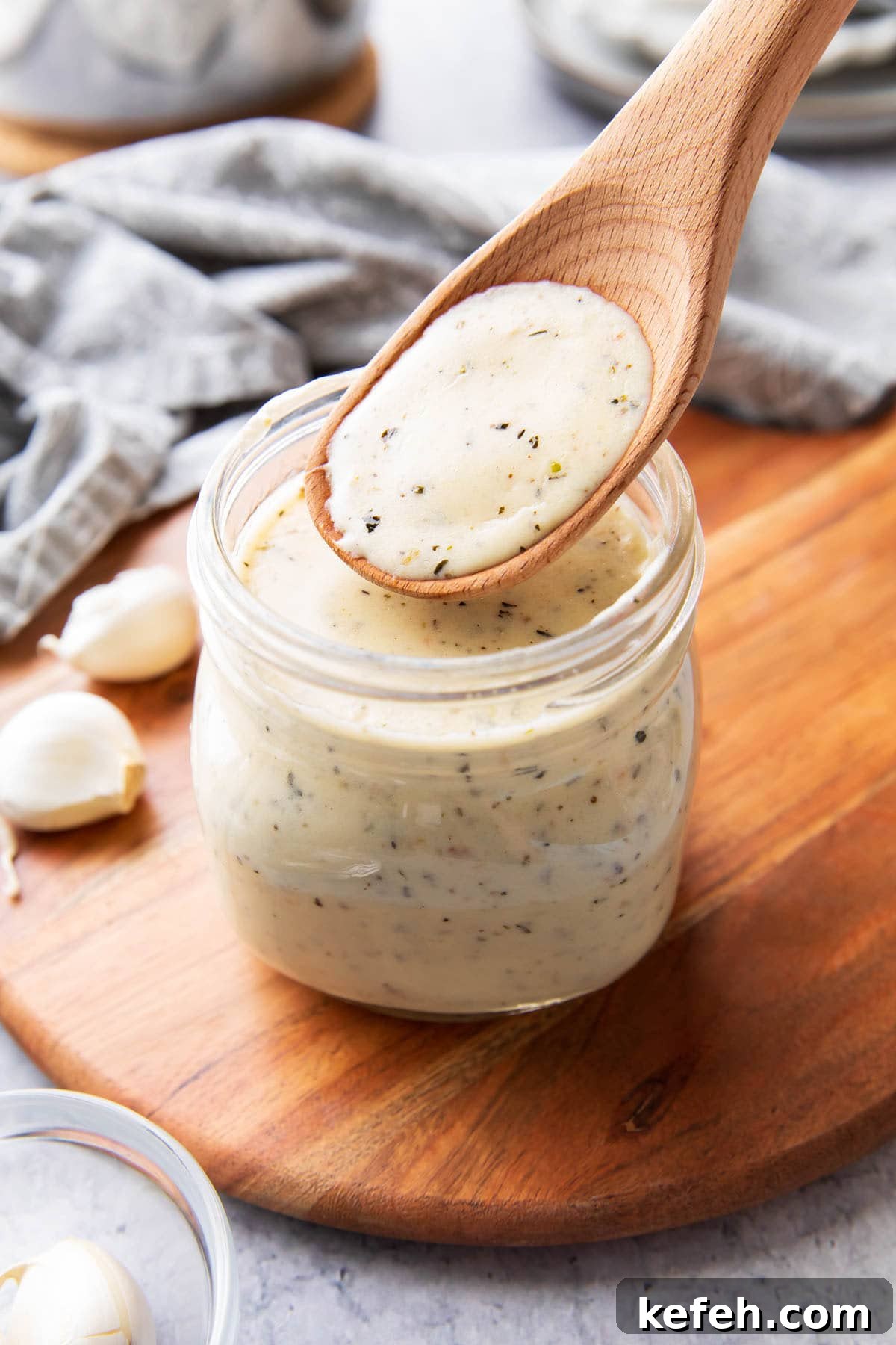 A wooden spoon filled with garlic parmesan sauce to showcase its thick and creamy texture that’s perfect for pouring over pasta, as a pizza sauce, and as wing sauce.