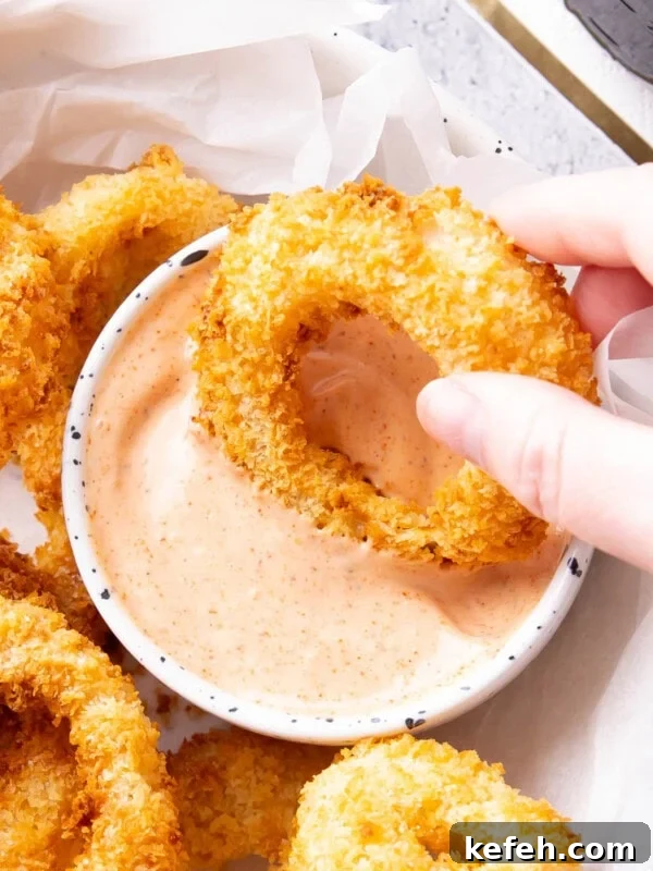 Hand dipping an onion ring into a bowl of onion ring sauce
