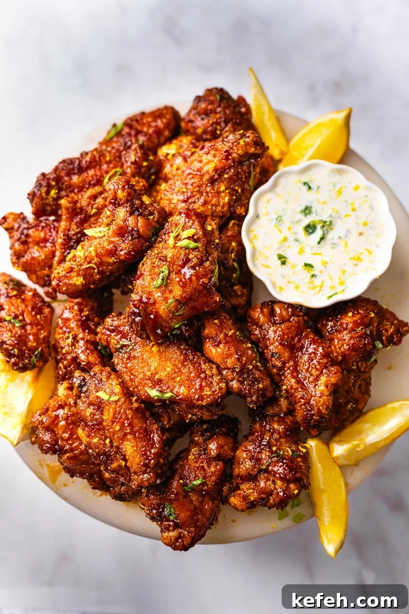 A plate of garlic soy chicken wings, garnished with green onions and lemon sauce with a side of ranch dressing.