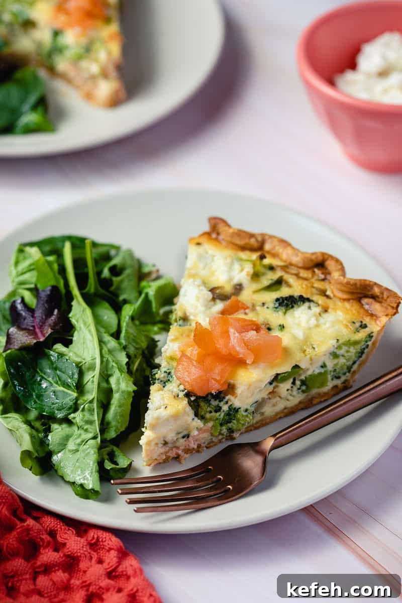 slice of salmon broccoli quiche next to salad greens and fork in front of other plate and bowl of goat cheese.