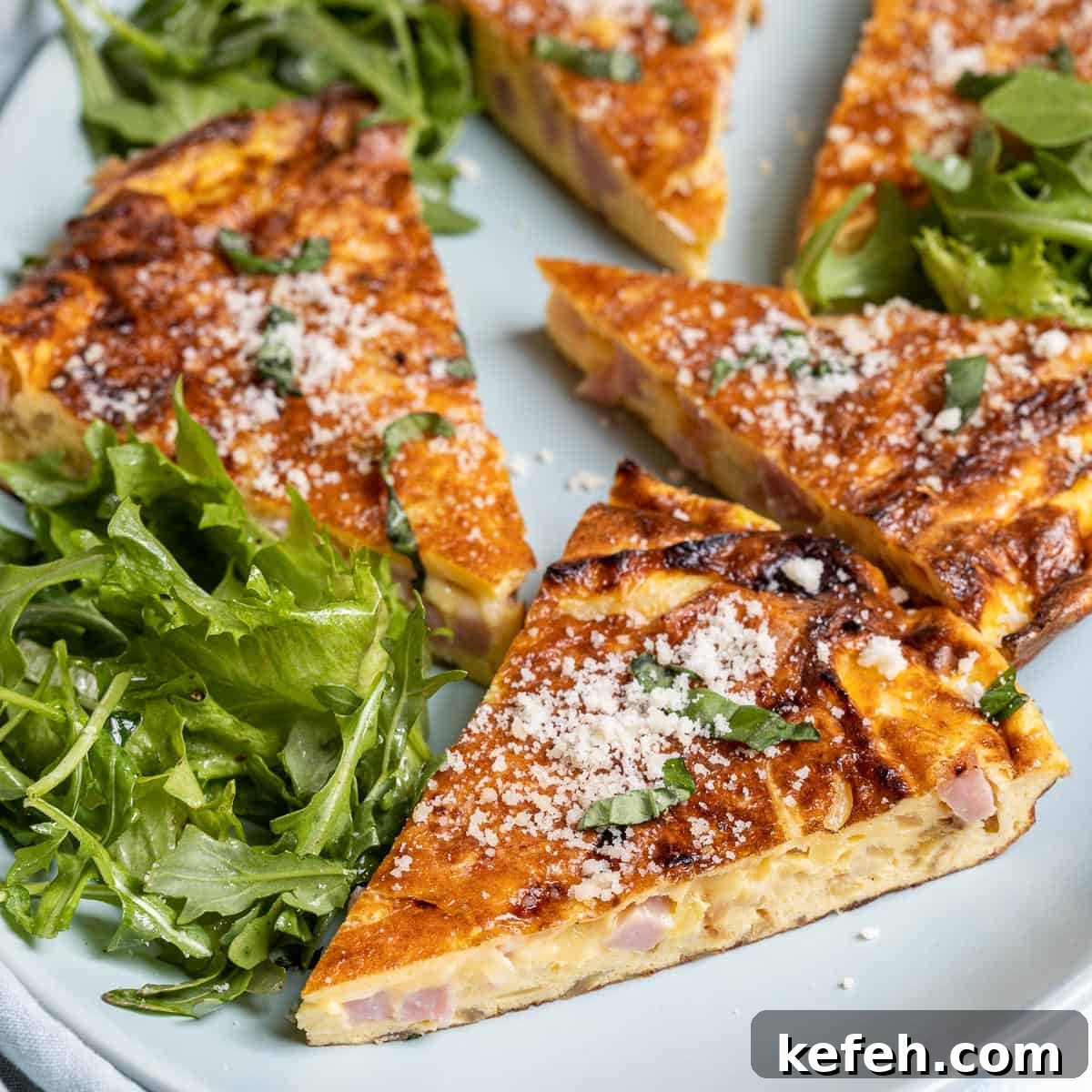 close up of slice of ham and cheese frittata on plate with salad greens and other slices in background