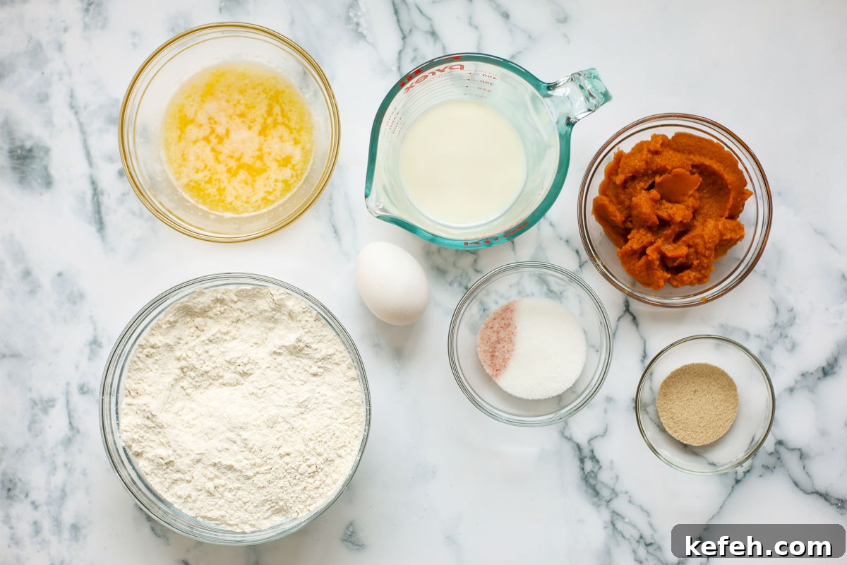 Ingredients of this recipe in glass bowls: melted butter, flour, milk, salt and sugar, yeast, pumpkin puree, and an egg.