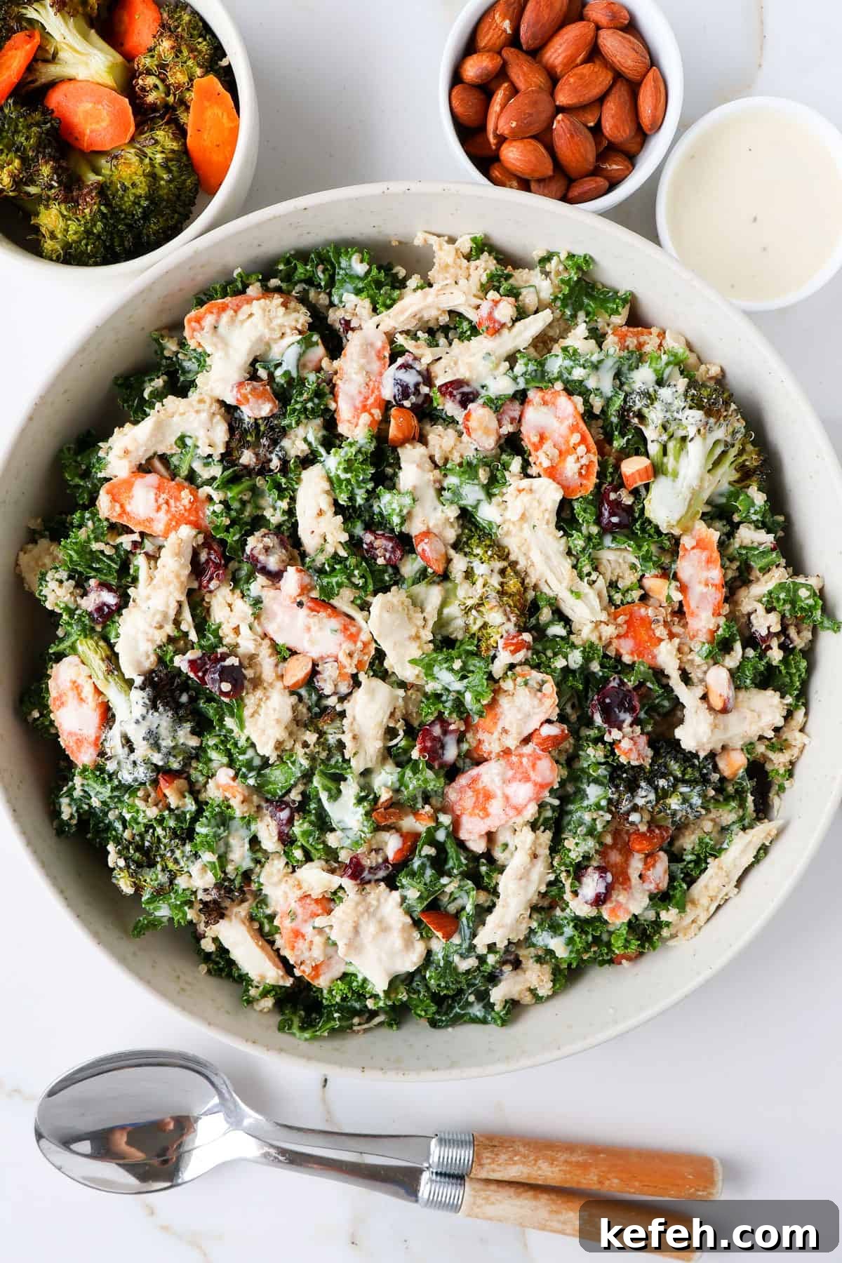 Chicken, broccoli and kale salad served in a bowl with spoons.