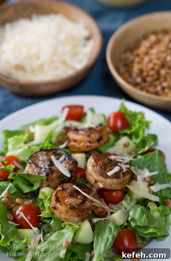 A white plate filled with a green salad, cucumbers, and tomatoes topped with grilled shrimp and garnished with cheese.