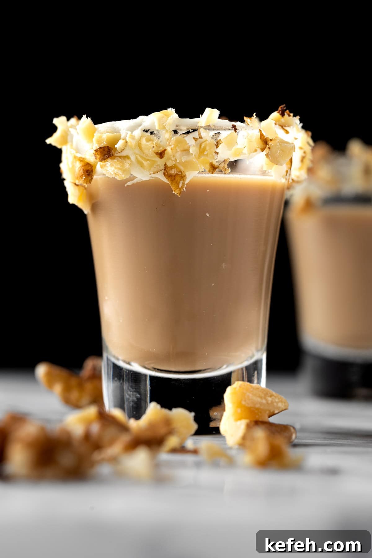 Carrot Cake Cocktail Shot Recipe — Creamy Spiced Dessert Shooter 2 A carrot cake shot with a cream cheese frosting and walnut rim, on a black background.