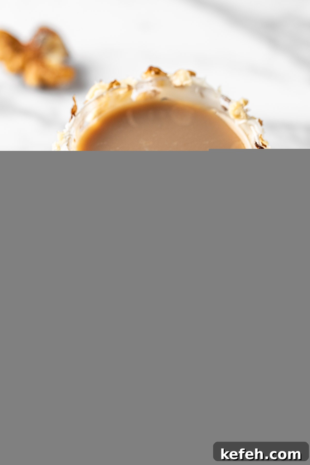 Carrot Cake Cocktail Shot Recipe — Creamy Spiced Dessert Shooter 6 A carrot cake shot with a frosted rim and walnut crumbles, on a white marble table.