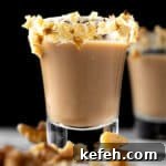 A carrot cake shot with a cream cheese frosting and walnut rim, on a black background.