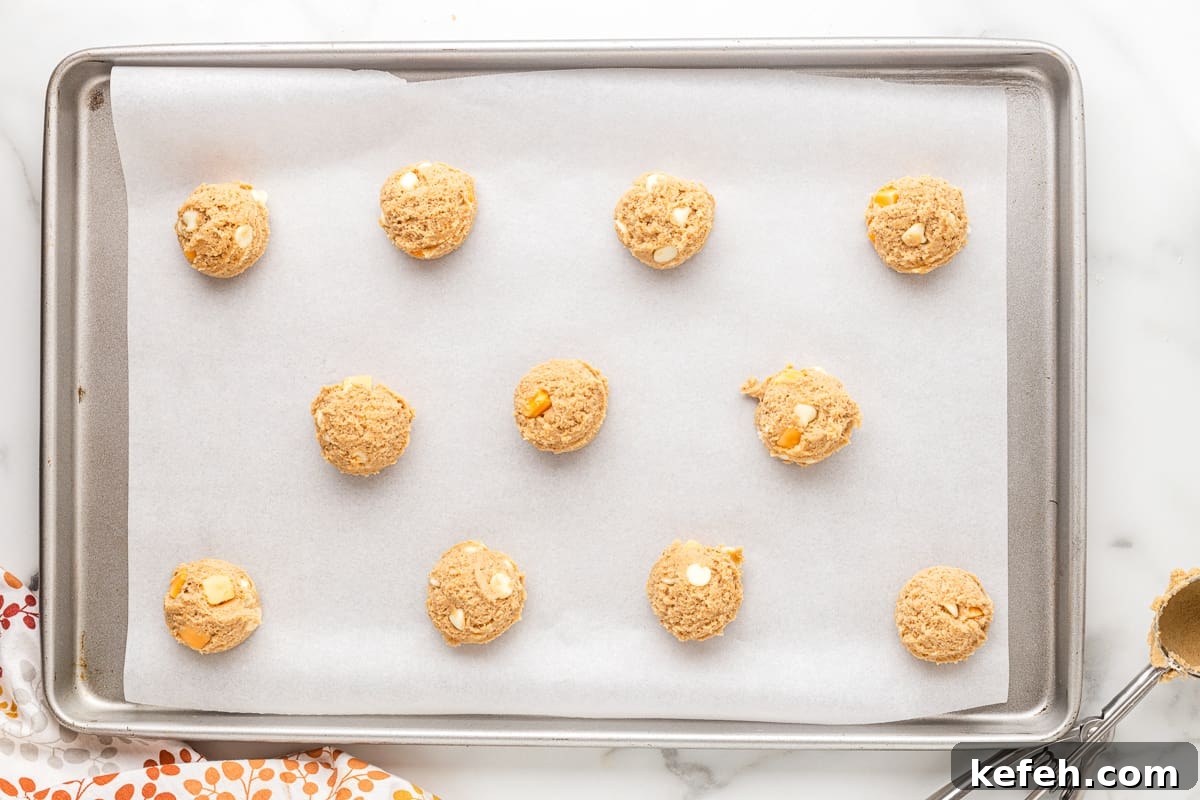 Balls of pumpkin spice cookie dough lined up on a baking sheet, before baking.