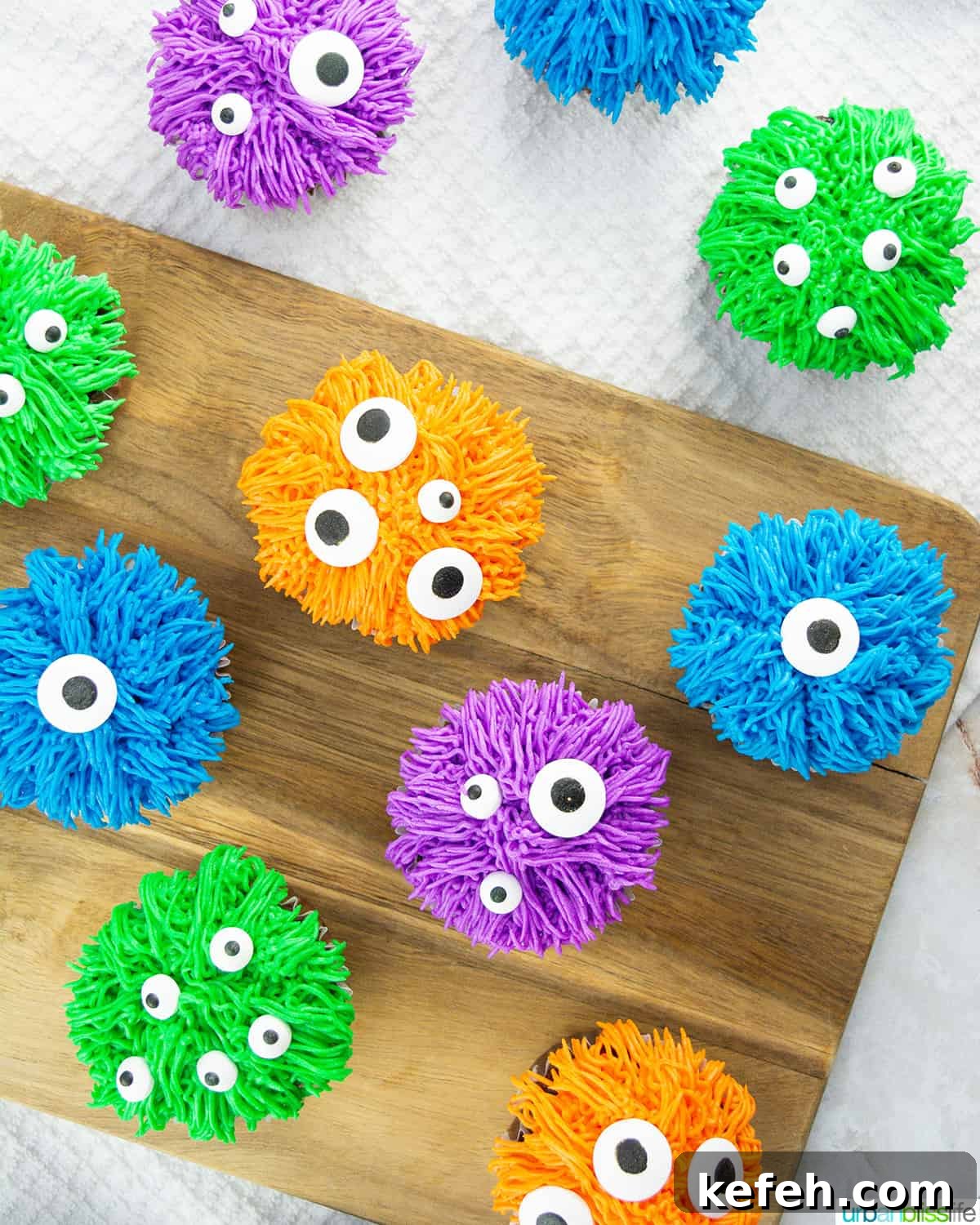 several colorful bright halloween monster cupcakes on a wood board.