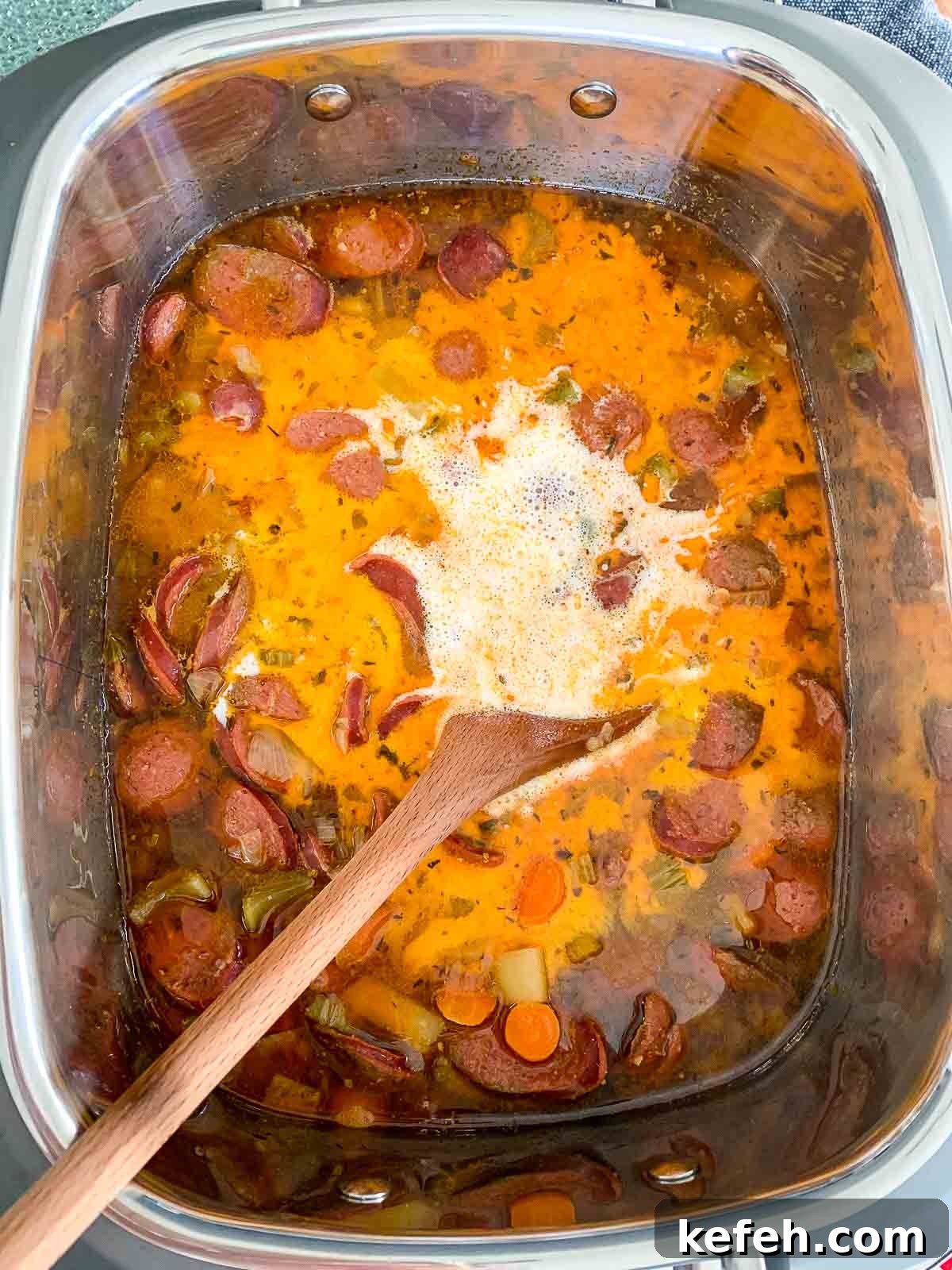 Slow cooker with ingredients and heavy cream being added.